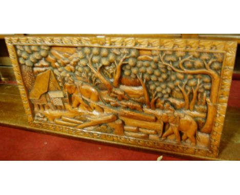An Indonesian stained and relief carved teak wall panel, depicting elephants within a landscape, 51 x 102cm