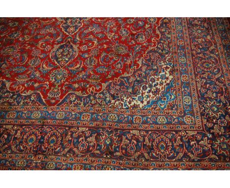 A Persian Keshan woollen carpet having a red ground with a central medallion issuing scroll flowers and foliage within multip