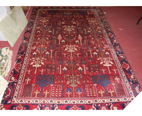 A Persian red ground woollen carpet, the central ground decorated with stylised trees within trailing tramline borders, 290x1