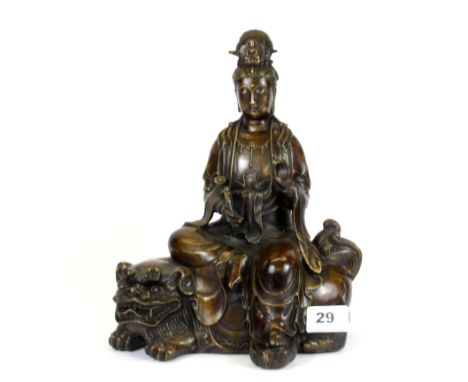 A Chinese bronze figure of the goddess Guanyin seated on a lion dog, with impressed six character mark to base, H. 28cm.