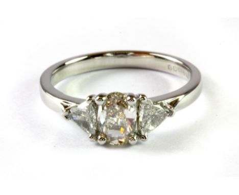 A platinum (hallmarked 950) ring set with a centre oval cut light orangy pink diamond and trillion cut diamond set shoulders,