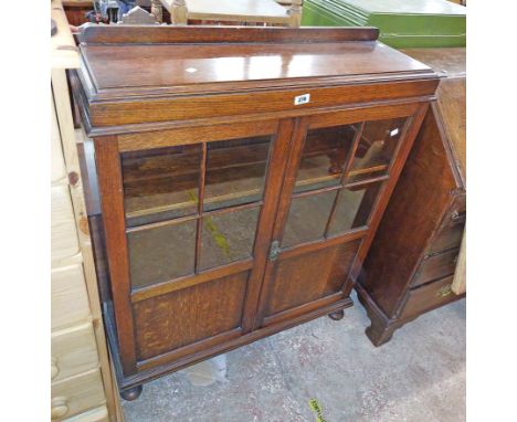 A 90cm vintage oak book cabinet with shelves enclosed by a pair of beaded glazed panel doors, set on bun feet