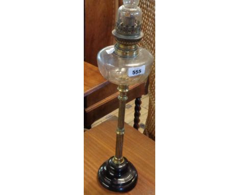 A Victorian oil lamp with reeded brass candlestick pillar, clear glass slice cut reservoir set on black ceramic base with cle