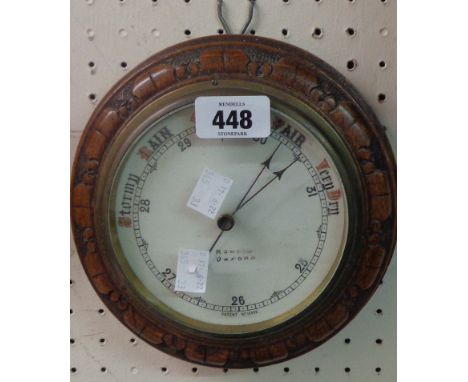 A late Victorian carved oak cased circular wall barometer with printed ceramic dial marked for Oxford retailer and with anero