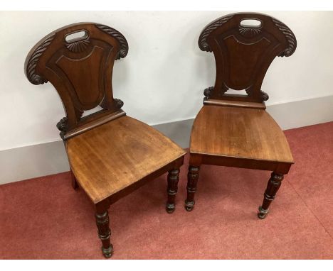 A Pair of William IV Mahogany Hall Chairs, with scroll and foliate decoration, panel back and solid seats on turned forefront