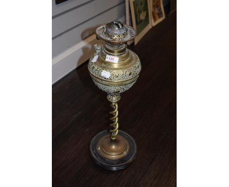 A late 19th century embossed brass oil lamp, having twist stem and wooden base, void of chimney.