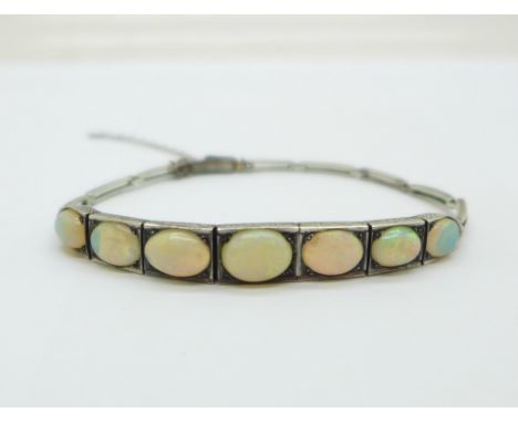 A c1900 white metal bracelet set with seven opals, the centre opal approximately 7mm x 9mm, safety chain requires repair 