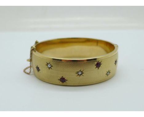A hallmarked 9ct gold bangle set with pearls and garnets, Birmingham 1965, Cropp &amp; Farr Ltd., 33g, 18mm wide 