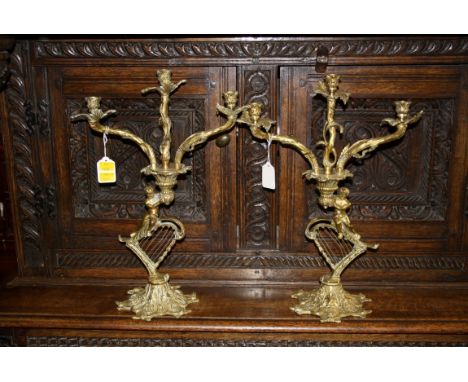 A pair of gilt brass rococo-style candelabra with cherub and harp detail, 42cm high