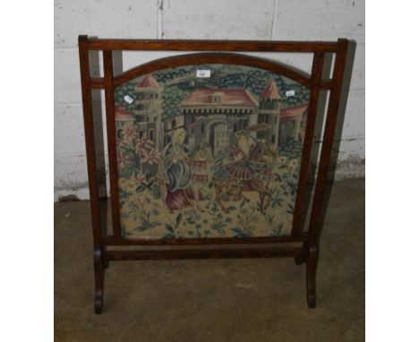 An Edwardian oak firescreen, the pierced frame enclosing a woolwork panel of Medieval figures on horseback, on splayed end fe