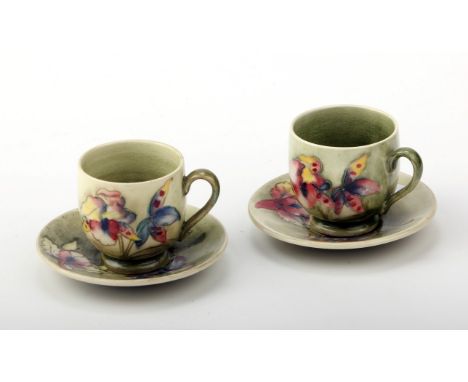 A pair of circa 1950's Moorcroft Orchid coffee cups and saucers, each with mutli coloured blooms on a shaded green ground. Im