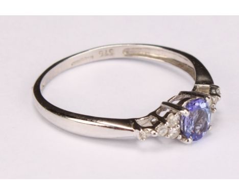 A tanzanite and white sapphire ring, the central blue oval facet cut stone flanked by 8 small round cut white stones, 9ct whi