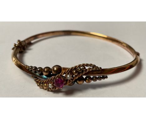 An Edwardian 9ct gold hinged bangle, set with seed pearl and ruby stones, marked 9ct, safety clasp, 6cm interior, 5.6g, boxed