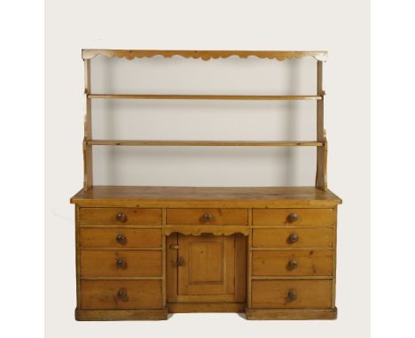 A VICTORIAN PINE KITCHEN DRESSER, with open shelf back and wavy edged cornice above an arrangement of drawers and a cupboard,