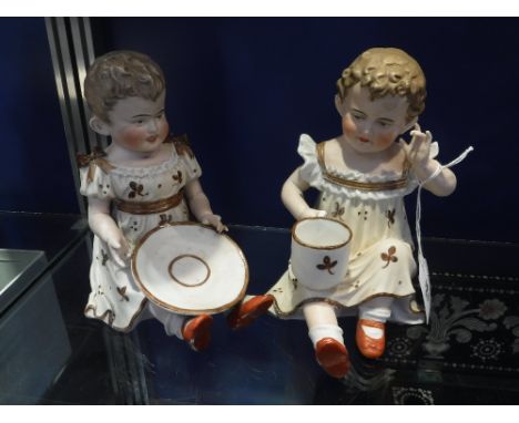 TWO CONTINENTAL CERAMIC MODELS OF SEATED CHILDREN holding a cup and saucer