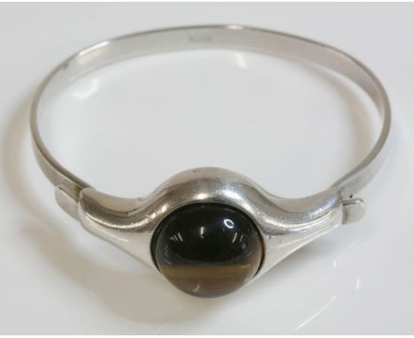 A Norwegian modernist silver tiger's eye bangle, c.1970, by A Holthe of Arandel, a circular cabochon tiger's eye, rub set to 