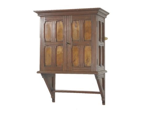 A walnut wall cabinet, in the style of E W Godwin, late 19th century, with panelled doors and sides, on an integral bracket b