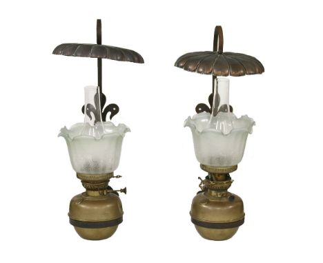 A pair of Arts and Crafts wrought iron, brass and copper oil lamps, with etched shades, a sinuous bracket and copper lily pon