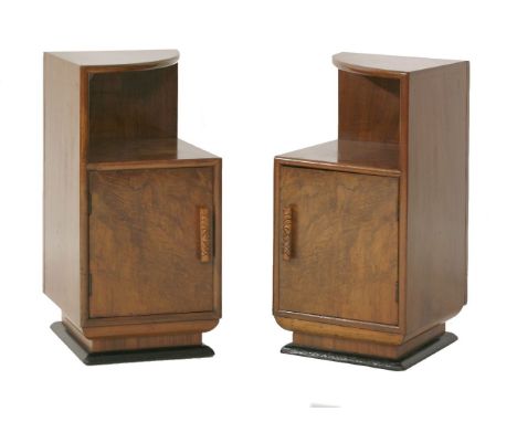 A pair of walnut pot cupboards, a quarter cut top over a shelf with a cupboard below, with carved handle and on a raised ebon