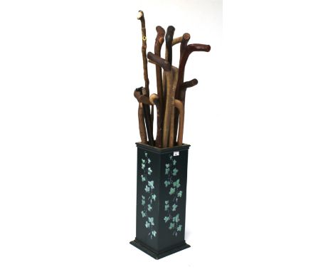 A stick stand with a collection of multiple walking sticks. The stand of rectangular form, painted in green with ivy decorati