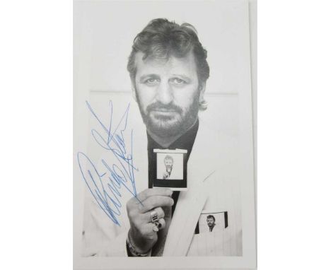 STARR, RINGO (1940 -) SIGNED POSTCARD PHOTO OF THE DRUMMER IN A HEAD AND SHOULDERS POSE wearing a white suit, holding a photo