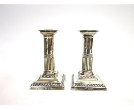 A PAIR OF EDWARDIAN SILVER DESK CANDLESTICKS by Goldsmiths and Silversmiths Co Ltd, London 1902, the square loaded base risin