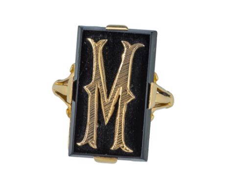 A yellow gold and onyx signet ring. The oblong onyx panel with a applied gold 'M', 20 x 10mm. Trifurcate shoulders. Finger si