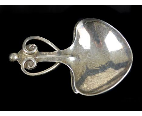 A.E Jones - An Arts and Crafts caddy spoon, the leaf shaped bowl of planished finish with a scrolled wire heart motif to hand