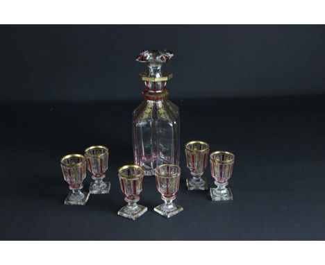 A French glass decanter and stopper with six conforming glasses, striped in ruby and embellished with gilded fruiting vines, 