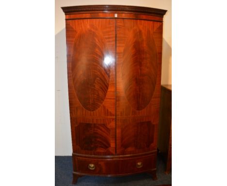 An Edwardian mahogany bow front wardrobe, with moulded cornice above two panelled doors and long drawer, raised on bracket su