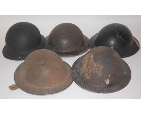 A WW II Brodie pattern steel helmet, with leather liner and canvas chin strap, together with four other WW II steel helmets. 