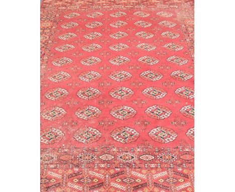 A Bokhara pattern carpet, 20th century, with multiple guls on a red field within broad geometric borders, 305cm x 202cm.Condi