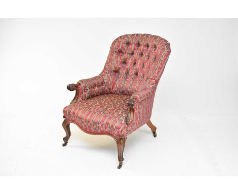 A late Victorian mahogany button-back armchair, the padded spoon back and arms with carved scroll show-wood over a padded sea