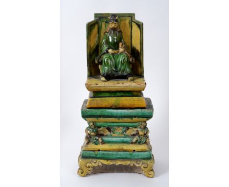 A Chinese sancai glazed figure of a wise Tao, holding a scroll and sitting on a throw, on a base decorated figures and scroll