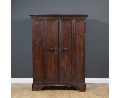 A continental stained pine cupboard with twin panelled doors and on carved bracket feet, opening to reveal a paper lined hang