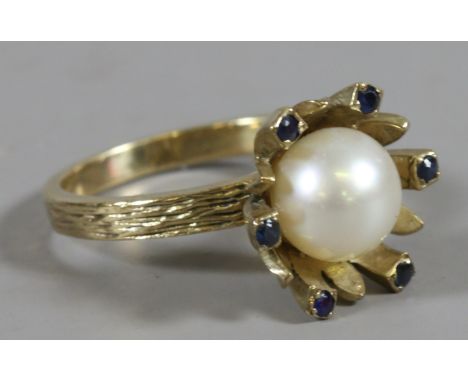 A 9ct gold designer ring set with a cultured pearl and sapphires in floriform setting. Assayed London 1968. 4.8 grams, size N