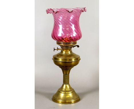 A brass based oil lamp with cranberry glass shade