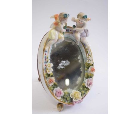 Small porcelain dressing table mirror of oval shape, the mirror surmounted by two cherubs with floral decoration