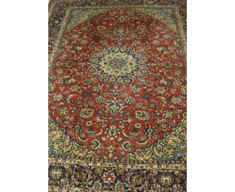 A Persian carpet, the central panel set with floral decorated medallion on a red ground with floral sprays within a stepped r