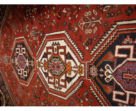 A Caucasian rug, the central panel set with three repeating medallions on a red ground with stylised floral decoration within