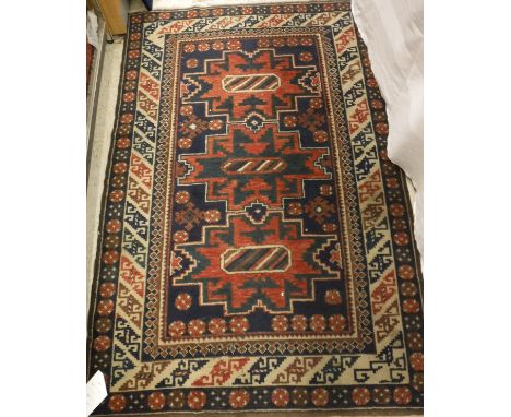 A Turkish rug of Lesghi design, the central panel set with three repeating medallions on a dark blue ground with a stylised f