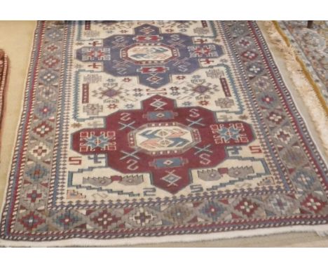 A Caucasian rug, the central panel set with three repeating medallions on a cream ground within a cream, red, blue and mushro