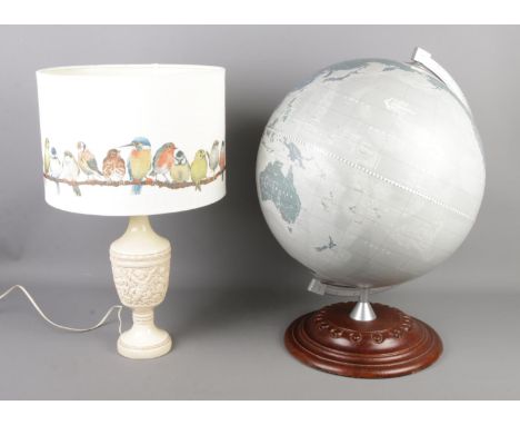 A large modern globe on carved turned base produced by Zoffoli Geografica, accompanied by a table lamp with cherubs to the bo