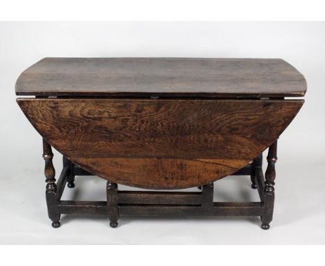 An early 18th century oak gate-leg dining table, the oval top on eight well shaped baluster turned and tapering supports unit