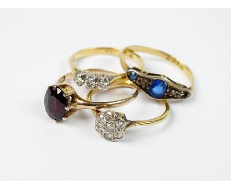 An early 20th century floral diamond cluster ring, together with a three stone diamond ring, a garnet ring and a blue paste r