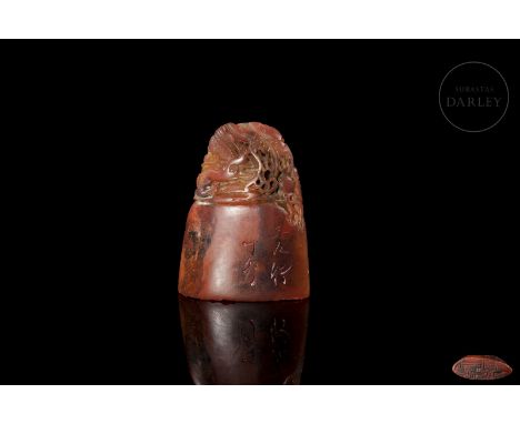 Carved Shoushan stone, with a deep reddish and amber colour. It has an elliptical base surmounted by the image of a ferocious
