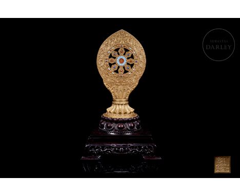 An enamelled porcelain figure modelled on one of the eight Buddhist treasures, known as the ‘Dharma Wheel’. It has a circular