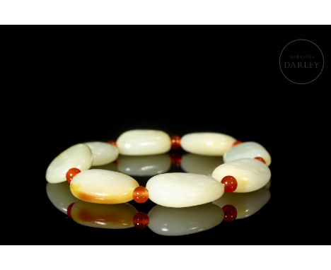 Carved white jade, with reddish and amber flecks. Each bead has an irregular, slightly oval shape and is decorated with incis