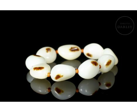 Nine carved white jade beads with brownish spots. They have an irregular, slightly oval shape, pierced by a hole through whic