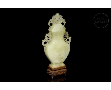 A beautifully carved jade vase in a light greenish hue. It has a flattened body that tapers into a slender flaring neck, flan